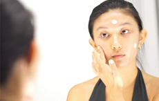 Woman applying sunscreen on her face in front of mirror